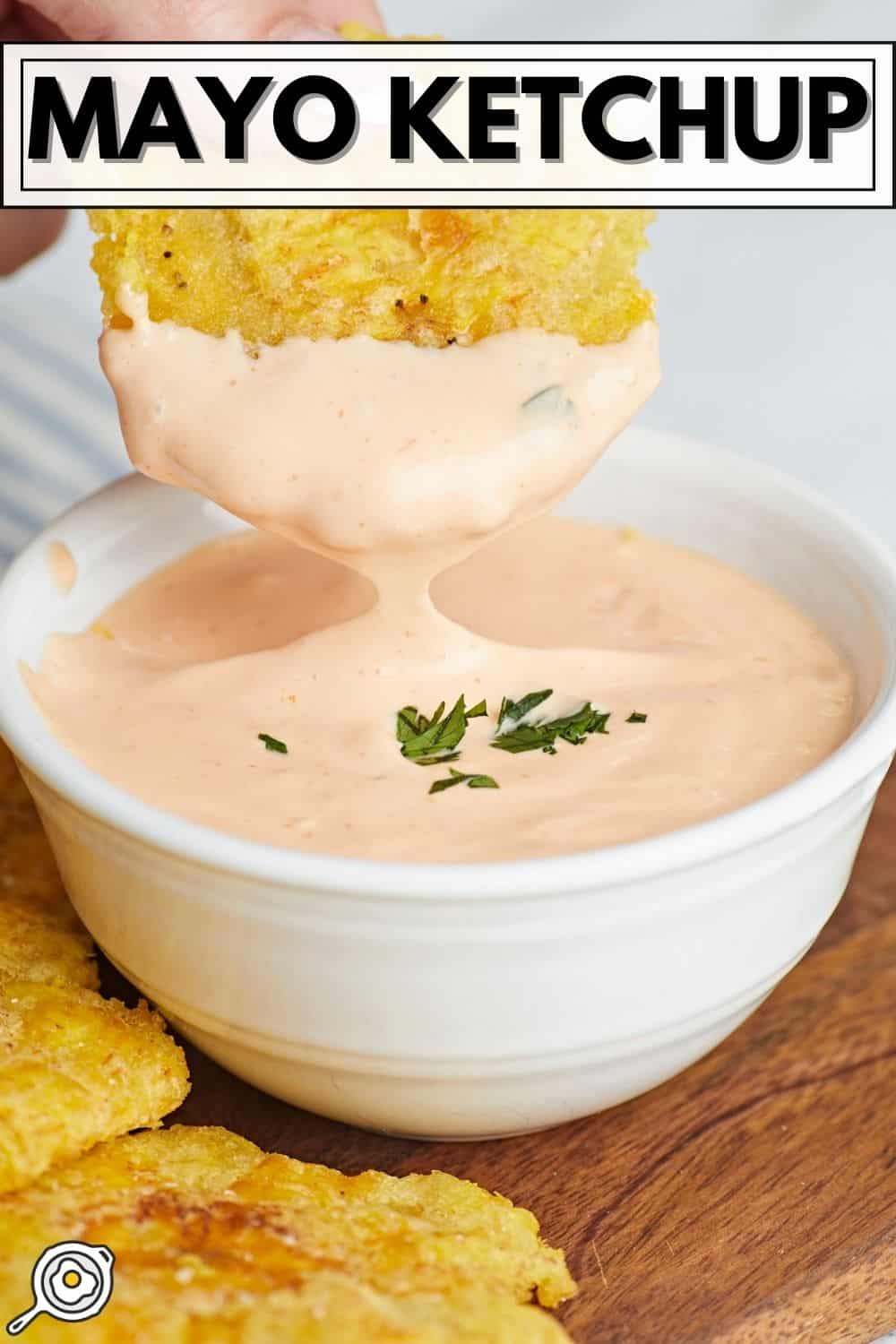 A close-up of a white bowl filled with creamy orange mayo ketchup, with a golden fried chip being dipped into the sauce. The text 'MAYO KETCHUP' appears at the top, and more chips are visible on a wooden surface. disponible en savia