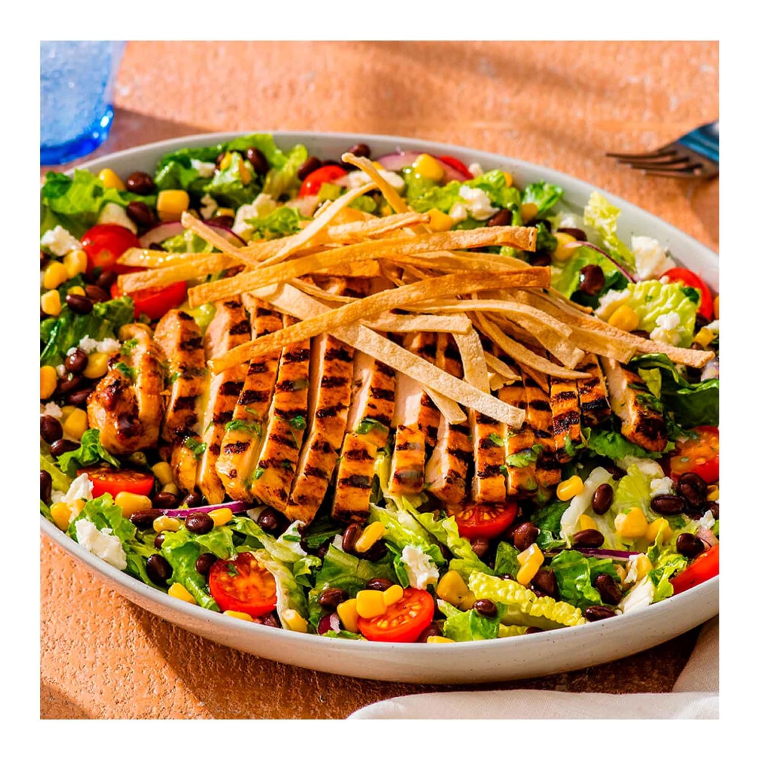 Colorful salad with grilled chicken, tortilla strips, and various vegetables on a white plate. make whith sazonador goya de Savia Farmacias