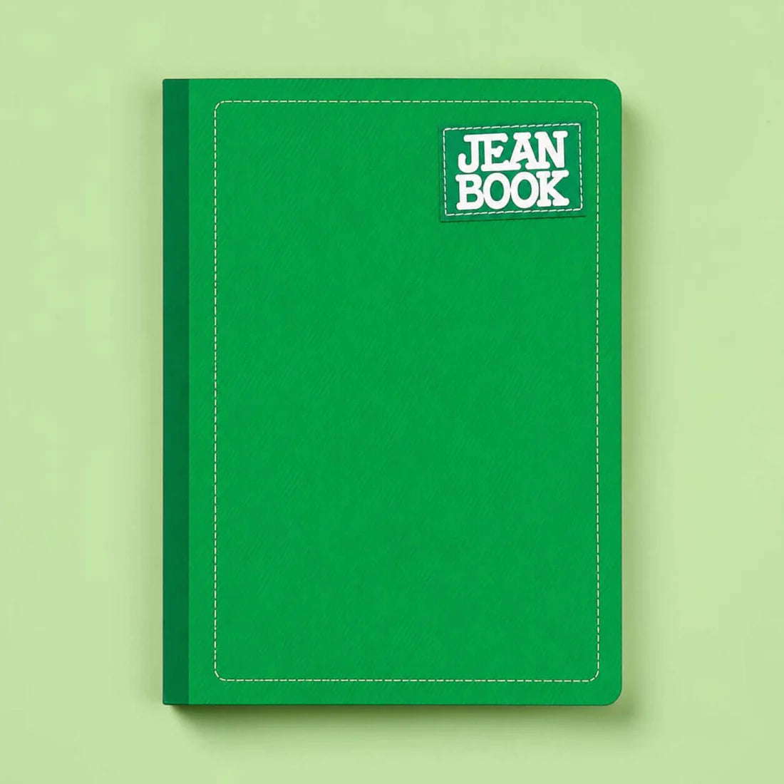 A green hardcover notebook with a white stitched border and a small 'JEAN BOOK' label on the top right, shown against a light green background.