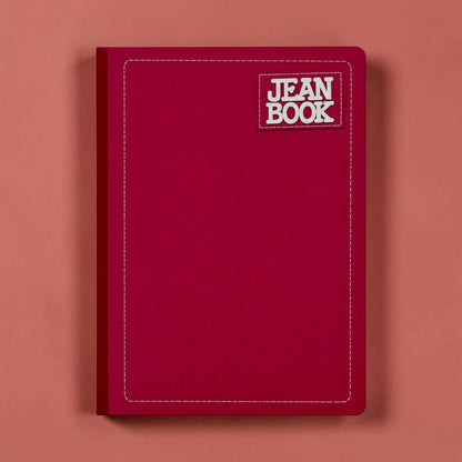 A dark red hardcover notebook with a white stitched border and a 'JEAN BOOK' logo patch on the top right, set against a solid coral-pink background.