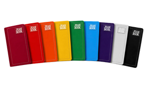 A row of colorful hardcover books or notebooks labeled 'JEAN BOOK' in white text, shown against a vivid rainbow paint-splatter background. The books are arranged in a fan shape and come in multiple colors including red, orange, yellow, green, blue, purple, white, and black.
