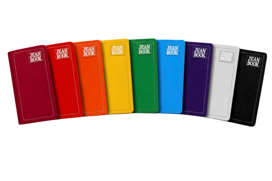 A row of colorful hardcover books or notebooks labeled 'JEAN BOOK' in white text, shown against a vivid rainbow paint-splatter background. The books are arranged in a fan shape and come in multiple colors including red, orange, yellow, green, blue, purple, white, and black.